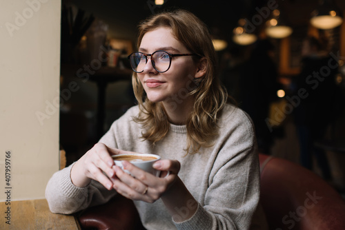 Pensive young woman with cup of hot drink in cafe