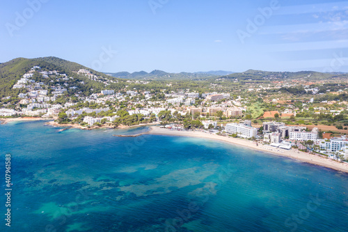 Aerial drone photo of the beautiful island of Ibiza in Spain showing the costal front golden sandy beaches with people relaxing and sunbathing on a hot sunny summers day