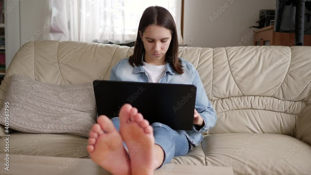 Teenager kid girl with laptop computer distance school work learning education at home on a couch