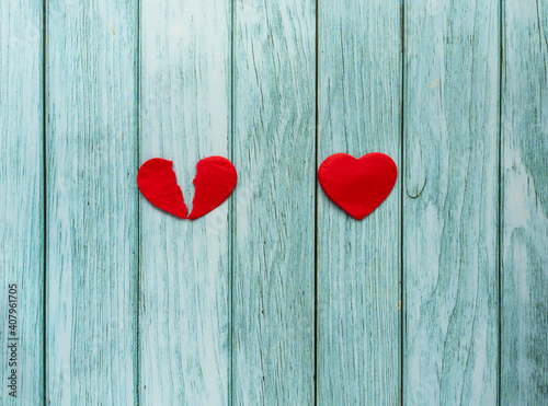 Two red hearts on wooden turquoise background. One heart is full and another heart is broken. Two different types of love stories concept.