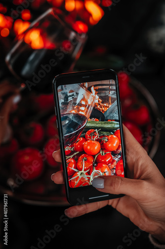 Closeup of women's hand making photo of food on mobile phone, female taking pictures with cell phone camera of delicious  burning grill fire, tomato and wine during rest.