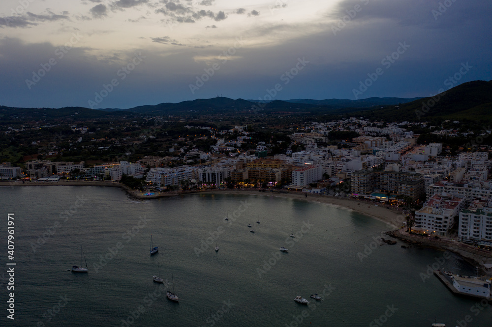Aerial photo of the beautiful town of Ibiza in Spain showing the town at sunset with the sun setting behind the mountains along the boating harbour in Santa Eularia des Riu