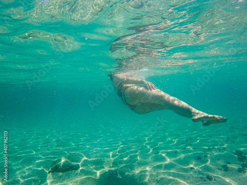 Young unrecognized woman with swimwear swimming underwater.