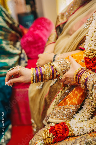 Close up indian pakistani bride hands with golden henna in yellow dress wearing many jewelry bracelets during mehndi wedding party