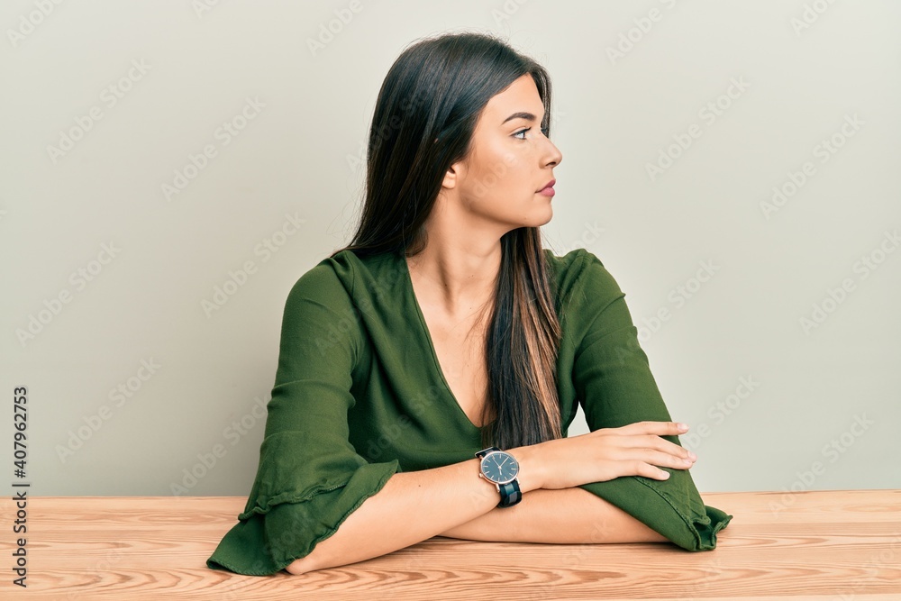 Young brunette woman wearing casual clothes sitting on the table looking to side, relax profile pose with natural face with confident smile. Young brunette woman wearing casual clothes sitting on the table looking to side, relax profile pose with natural face with confident smile.