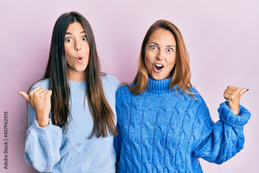 Hispanic family of mother and daughter wearing wool winter sweater surprised pointing with hand finger to the side, open mouth amazed expression. Hispanic family of mother and daughter wearing wool winter sweater surprised pointing with hand finger to the side, open mouth amazed expression.