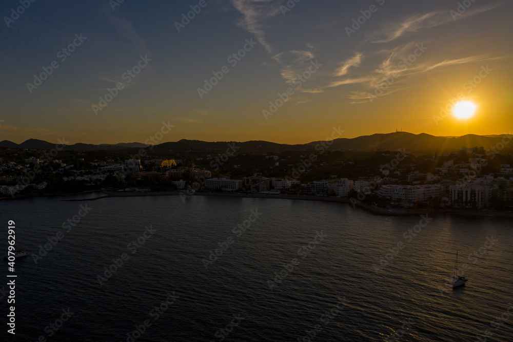 Aerial photo of the beautiful town of Ibiza in Spain showing the town at sunset with the sun setting behind the mountains along the boating harbour in Santa Eularia des Riu