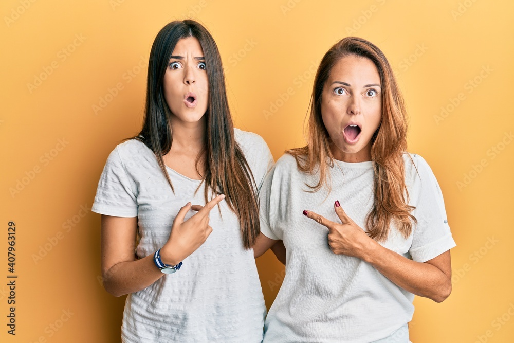 Hispanic family of mother and daughter wearing casual white tshirt surprised pointing with finger to the side, open mouth amazed expression. Hispanic family of mother and daughter wearing casual white tshirt surprised pointing with finger to the side, open mouth amazed expression.