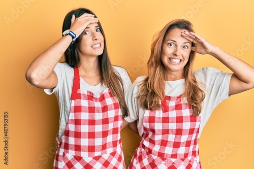 Hispanic family of mother and daughter wearing baker uniform over yellow background stressed and frustrated with hand on head, surprised and angry face