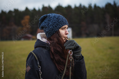 A young breeder in winter clothes blows a dog whistle to summon a stray dog. Authentic people. Binary portrait of girls aged 20-24 whistling at Barbu tcheque, Czech hunting breed photo