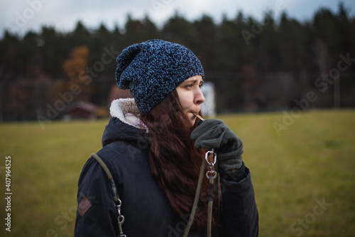 A young breeder in winter clothes blows a dog whistle to summon a stray dog. Authentic people. Binary portrait of girls aged 20-24 whistling at Barbu tcheque, Czech hunting breed