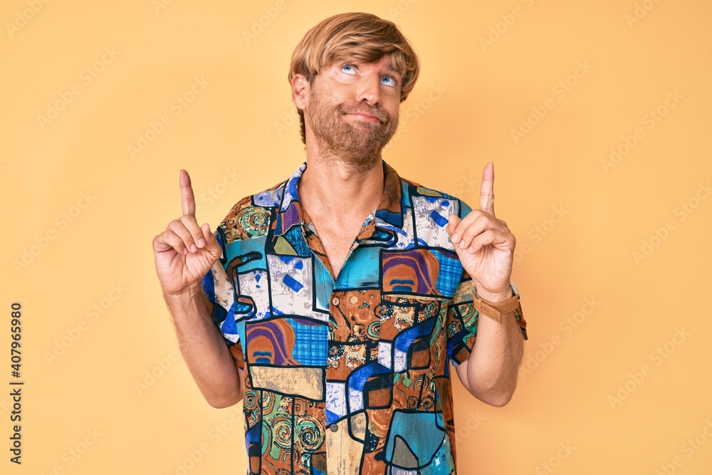 Young blond man wearing summer shirt pointing up looking sad and upset, indicating direction with fingers, unhappy and depressed.