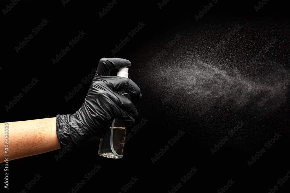 Close up view of human hand, black medical glove and antiseptic spray with splashes on black background. Hand sanitation. Epidemic control. Prevention of coronavirus. Selective focus.