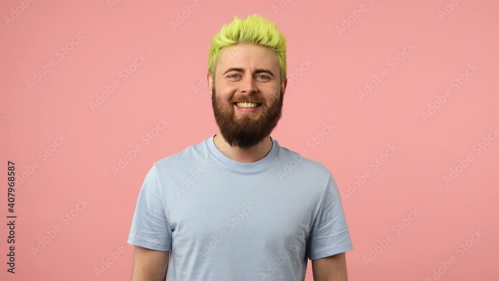 Portrait of positive bearded man with dyed bright green hair smiling and winking looking at camera, flirting, good mood. Indoor studio shot isolated on pink background Portrait of positive bearded man with dyed bright green hair smiling and winking looking at camera, flirting, good mood. Indoor studio shot isolated on pink background