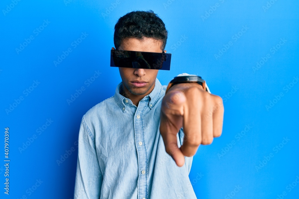 Fototapeta premium Young handsome african american man wearing banner glasses covering eyes pointing with finger to the camera and to you, confident gesture looking serious