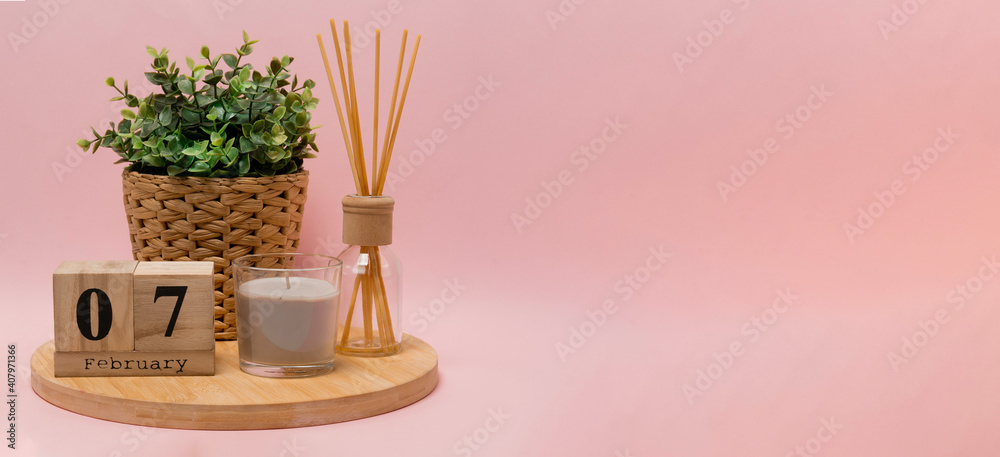 calendar. 7 february composition from a wooden calendar, a flower in a wicker pot, a gray candle in a glass candlestick and an aroma diffuser on a light pink background banner business calendar. 7 february composition from a wooden calendar, a flower in a wicker pot, a gray candle in a glass candlestick and an aroma diffuser on a light pink background banner business