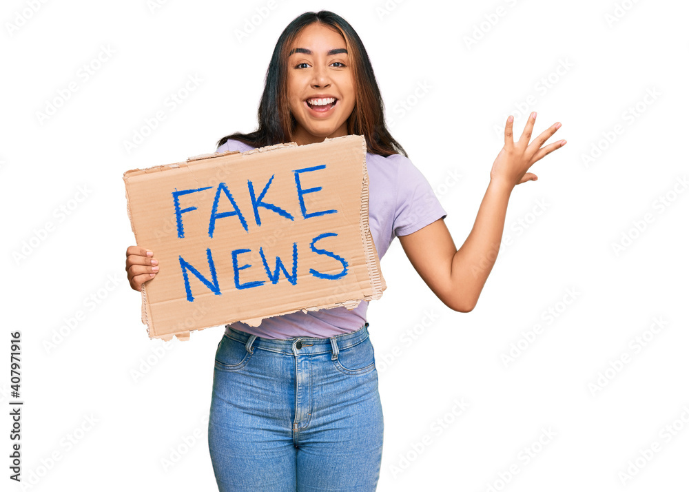 Young latin woman holding fake news banner celebrating victory with happy smile and winner expression with raised hands Young latin woman holding fake news banner celebrating victory with happy smile and winner expression with raised hands