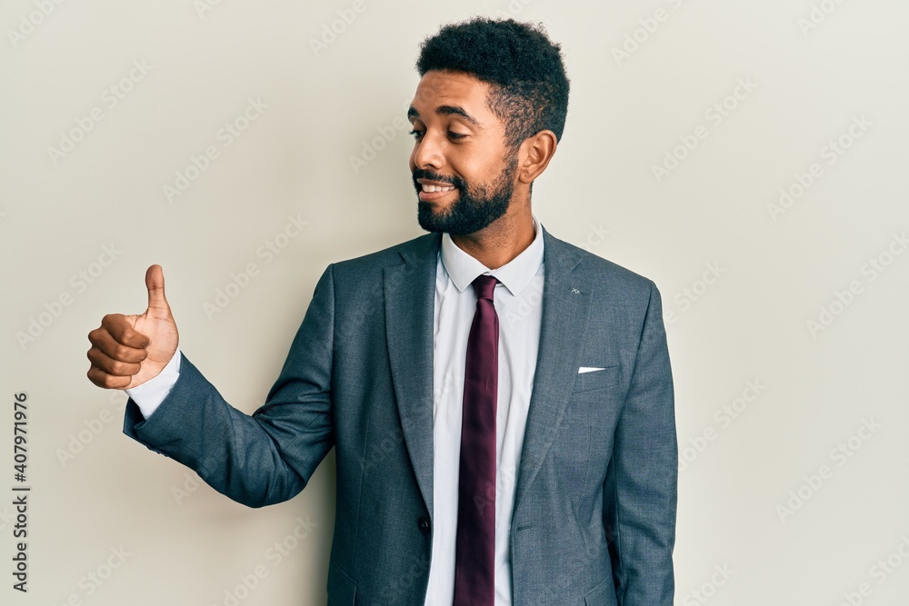 Handsome hispanic man with beard wearing business suit and tie looking proud, smiling doing thumbs up gesture to the side Handsome hispanic man with beard wearing business suit and tie looking proud, smiling doing thumbs up gesture to the side