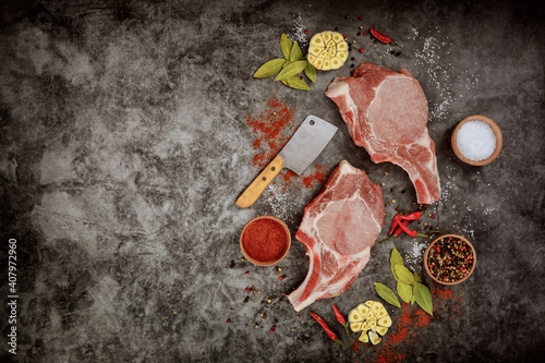 Raw pork chops with spices and cleaver on dark background.