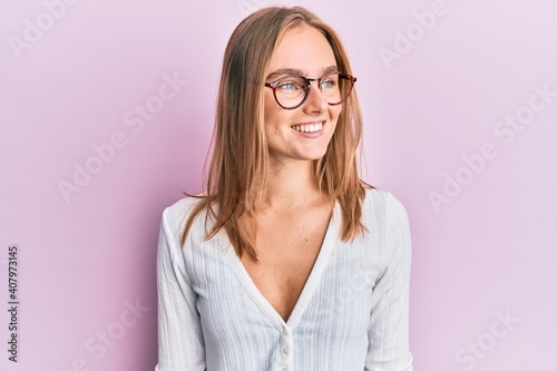 Beautiful blonde woman wearing casual clothes and glasses looking to side, relax profile pose with natural face and confident smile.