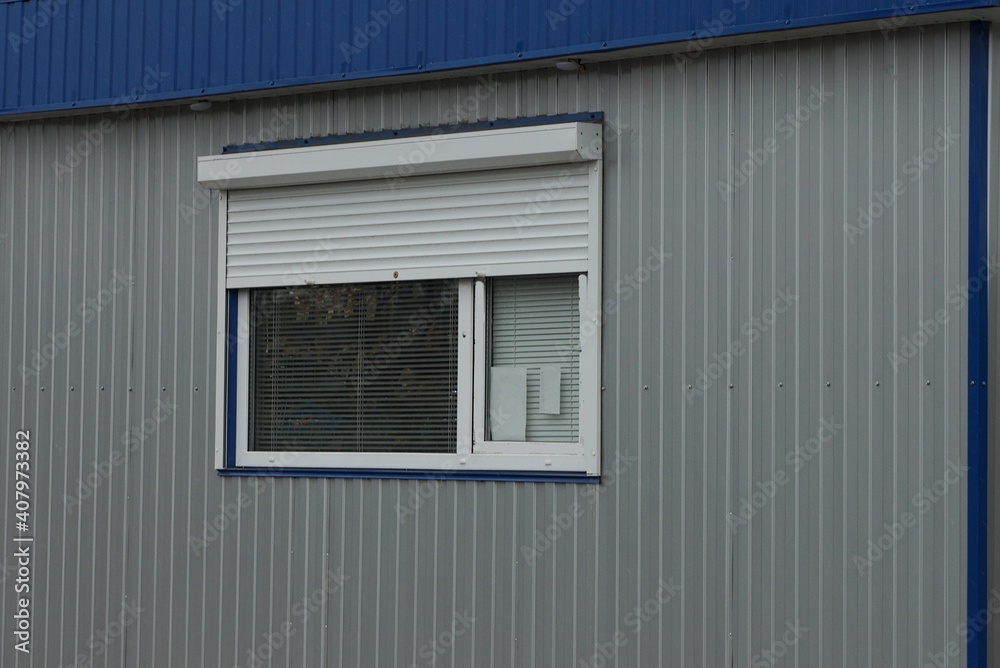 one window with white blinds on a gray metal wall of a building on the street