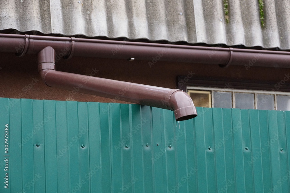 one long brown plastic gutter pipe on green metal fence wall outside