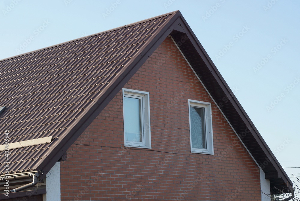 brown bricks attic of a private house with windows under a tiled roof against a blue sky brown bricks attic of a private house with windows under a tiled roof against a blue sky