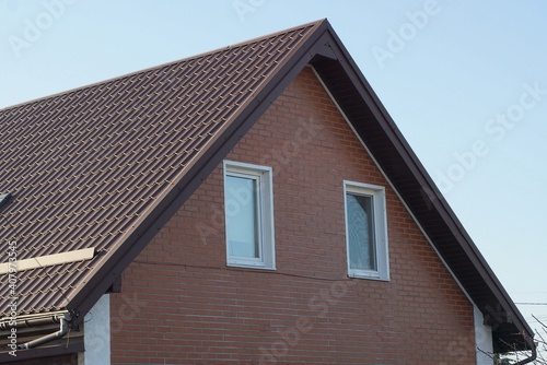 brown bricks attic of a private house with windows under a tiled roof against a blue sky