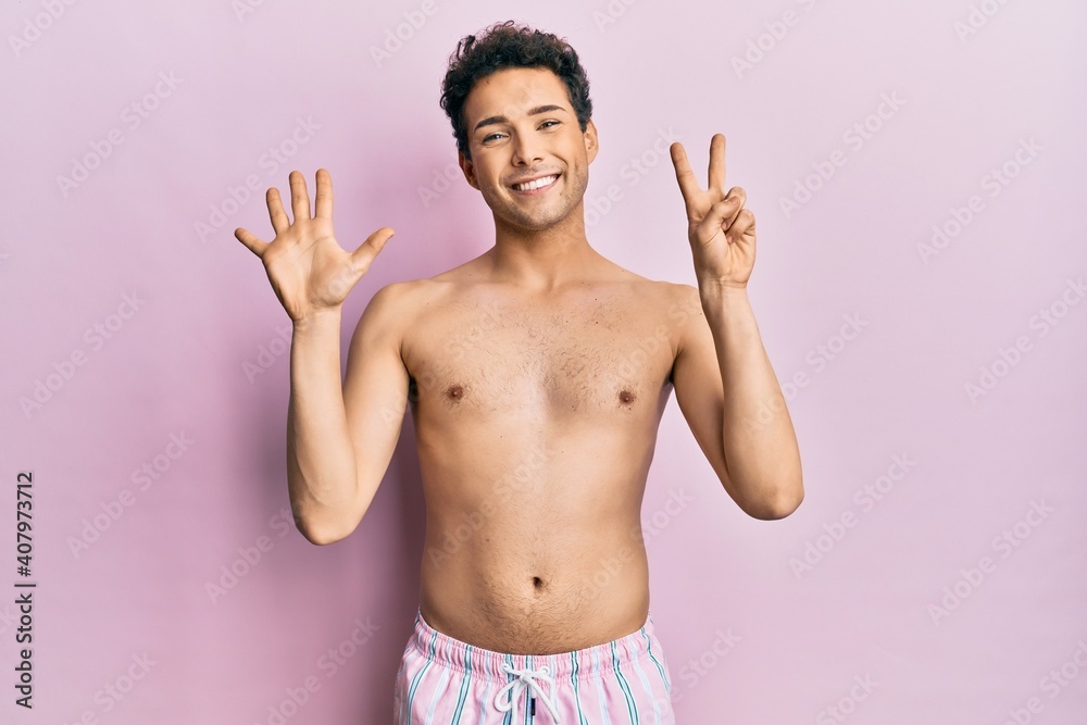 Fototapeta premium Young handsome man wearing swimwear shirtless showing and pointing up with fingers number seven while smiling confident and happy.