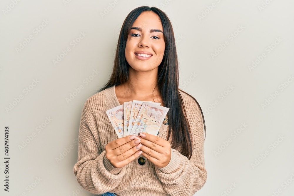 Young beautiful hispanic girl holding 10 united kingdom pounds banknotes smiling with a happy and cool smile on face. showing teeth. Young beautiful hispanic girl holding 10 united kingdom pounds banknotes smiling with a happy and cool smile on face. showing teeth.