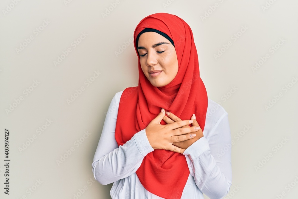 Young beautiful hispanic girl wearing traditional islamic hijab scarf smiling with hands on chest with closed eyes and grateful gesture on face. health concept. Young beautiful hispanic girl wearing traditional islamic hijab scarf smiling with hands on chest with closed eyes and grateful gesture on face. health concept.
