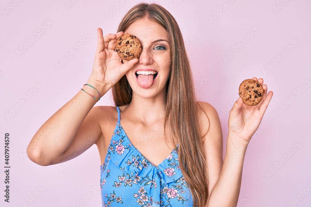 Young blonde girl holding cookie sticking tongue out happy with funny expression. Young blonde girl holding cookie sticking tongue out happy with funny expression.