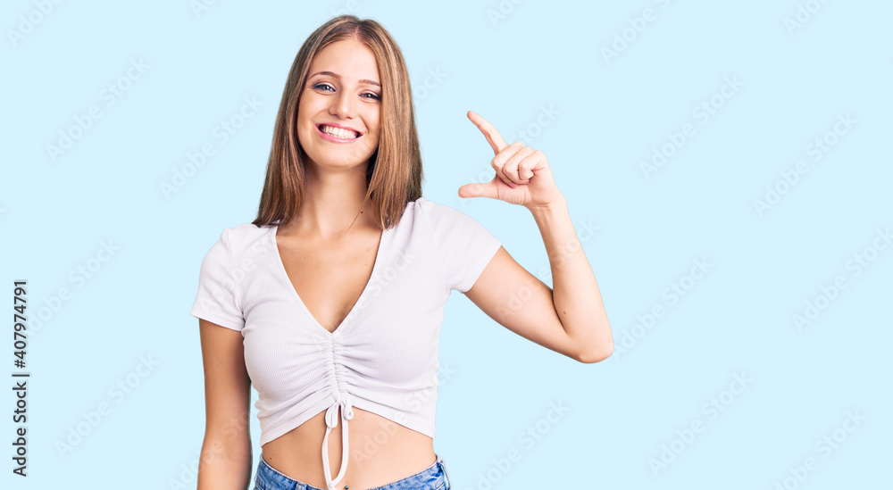 Young beautiful blonde woman wearing casual white tshirt smiling and confident gesturing with hand doing small size sign with fingers looking and the camera. measure concept. Young beautiful blonde woman wearing casual white tshirt smiling and confident gesturing with hand doing small size sign with fingers looking and the camera. measure concept.