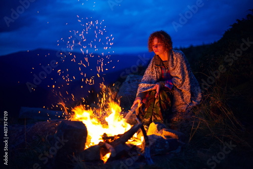Young caucasian woman near the bonfire at night in the mountains.