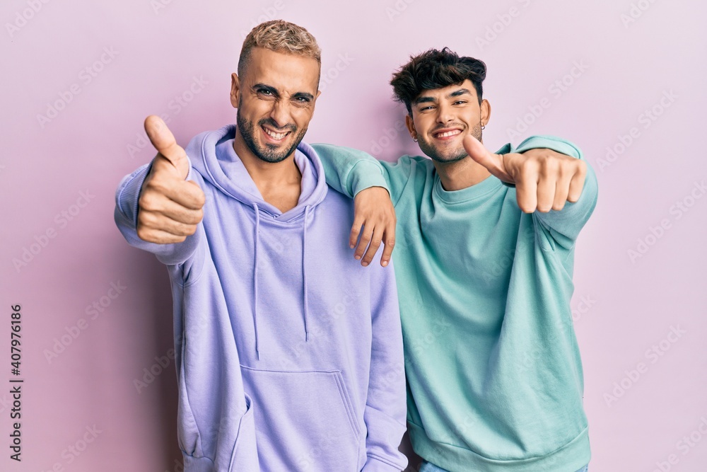 Homosexual gay couple standing together wearing casual clothes approving doing positive gesture with hand, thumbs up smiling and happy for success. winner gesture. Homosexual gay couple standing together wearing casual clothes approving doing positive gesture with hand, thumbs up smiling and happy for success. winner gesture.