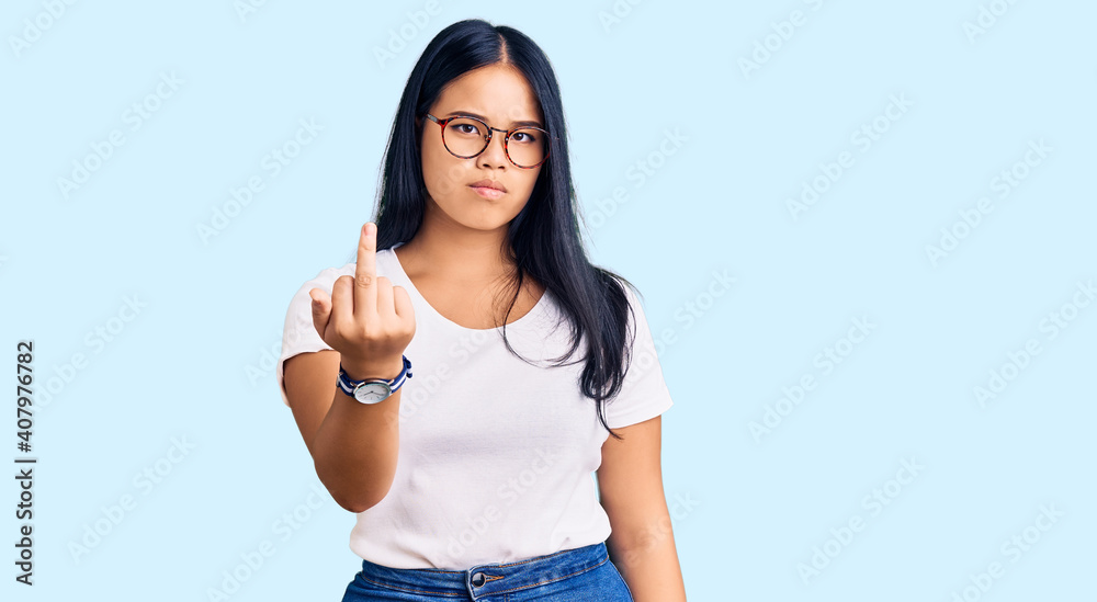 Young beautiful asian girl wearing casual clothes and glasses showing middle finger, impolite and rude fuck off expression Young beautiful asian girl wearing casual clothes and glasses showing middle finger, impolite and rude fuck off expression