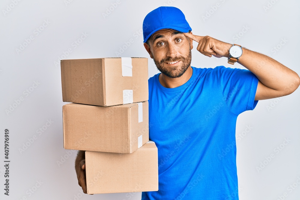 Handsome man with beard wearing courier uniform holding delivery packages smiling pointing to head with one finger, great idea or thought, good memory Handsome man with beard wearing courier uniform holding delivery packages smiling pointing to head with one finger, great idea or thought, good memory