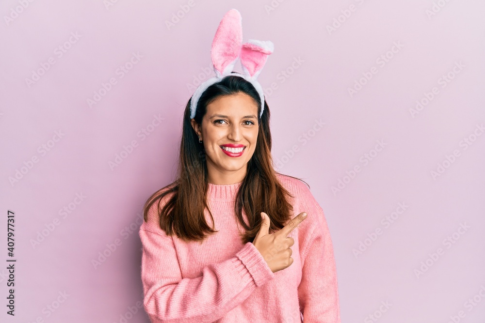Beautiful hispanic woman wearing cute easter bunny ears smiling cheerful pointing with hand and finger up to the side Beautiful hispanic woman wearing cute easter bunny ears smiling cheerful pointing with hand and finger up to the side