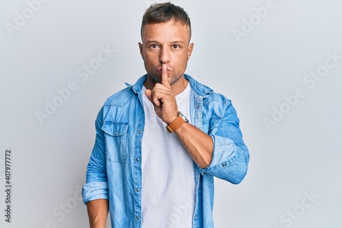 Handsome muscle man wearing casual denim jacket asking to be quiet with finger on lips. silence and secret concept.