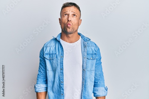 Handsome muscle man wearing casual denim jacket making fish face with lips, crazy and comical gesture. funny expression.