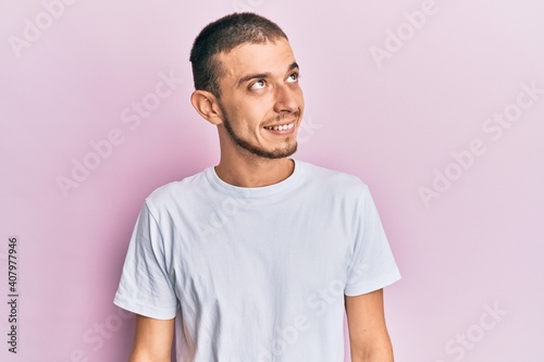 Hispanic young man wearing casual white t shirt looking to side, relax profile pose with natural face and confident smile.