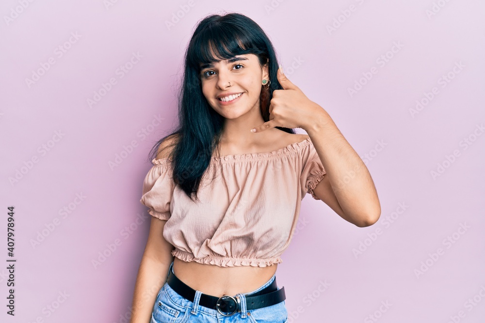 Young hispanic girl wearing casual clothes smiling doing phone gesture with hand and fingers like talking on the telephone. communicating concepts. Young hispanic girl wearing casual clothes smiling doing phone gesture with hand and fingers like talking on the telephone. communicating concepts.