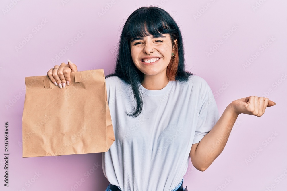 Young hispanic girl holding take away paper bag screaming proud, celebrating victory and success very excited with raised arm Young hispanic girl holding take away paper bag screaming proud, celebrating victory and success very excited with raised arm