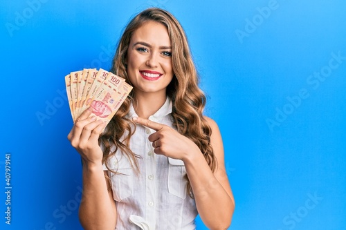 Young blonde girl holding mexican pesos smiling happy pointing with hand and finger photo