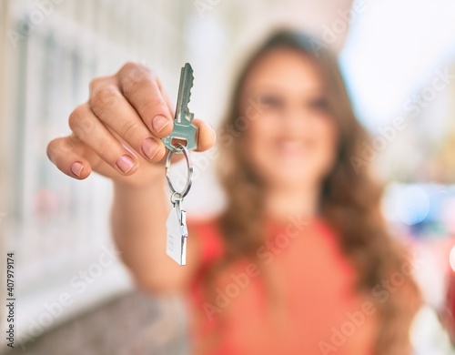 Young blonde girl smiling happy holding key of new house standing at the city.