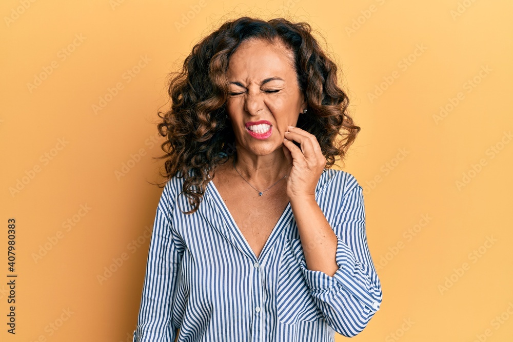 Middle age hispanic woman wearing casual clothes touching mouth with hand with painful expression because of toothache or dental illness on teeth. dentist Middle age hispanic woman wearing casual clothes touching mouth with hand with painful expression because of toothache or dental illness on teeth. dentist