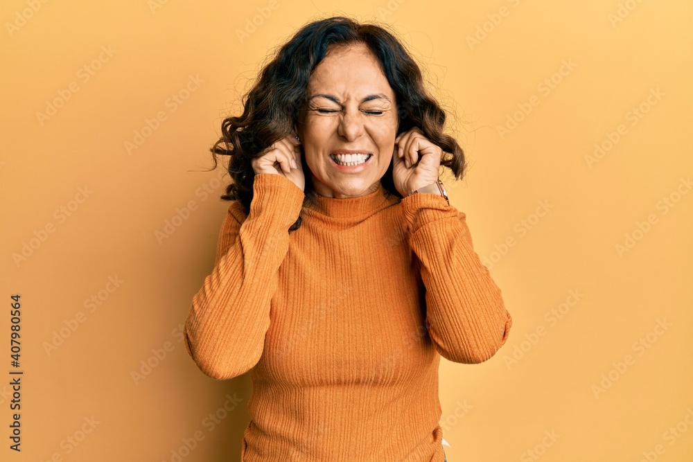 Middle age hispanic woman wearing casual clothes covering ears with fingers with annoyed expression for the noise of loud music. deaf concept. Middle age hispanic woman wearing casual clothes covering ears with fingers with annoyed expression for the noise of loud music. deaf concept.