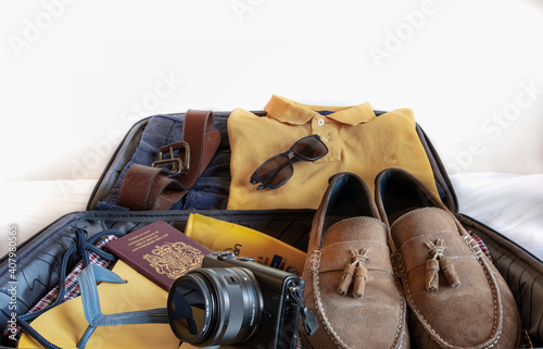 Photograph in landscapeformat of a suitcase packed with shorts, flip flops, gentlemans suede loafers, camera, sunglasses and sun cream