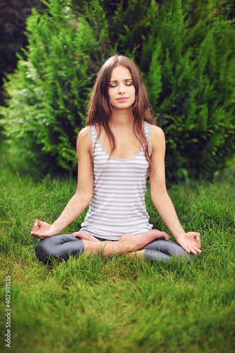 Young caucasian woman practicing yoga on the grass in the park photo