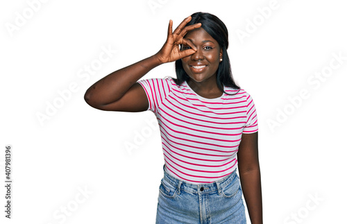 African young woman wearing casual striped t shirt doing ok gesture with hand smiling, eye looking through fingers with happy face.